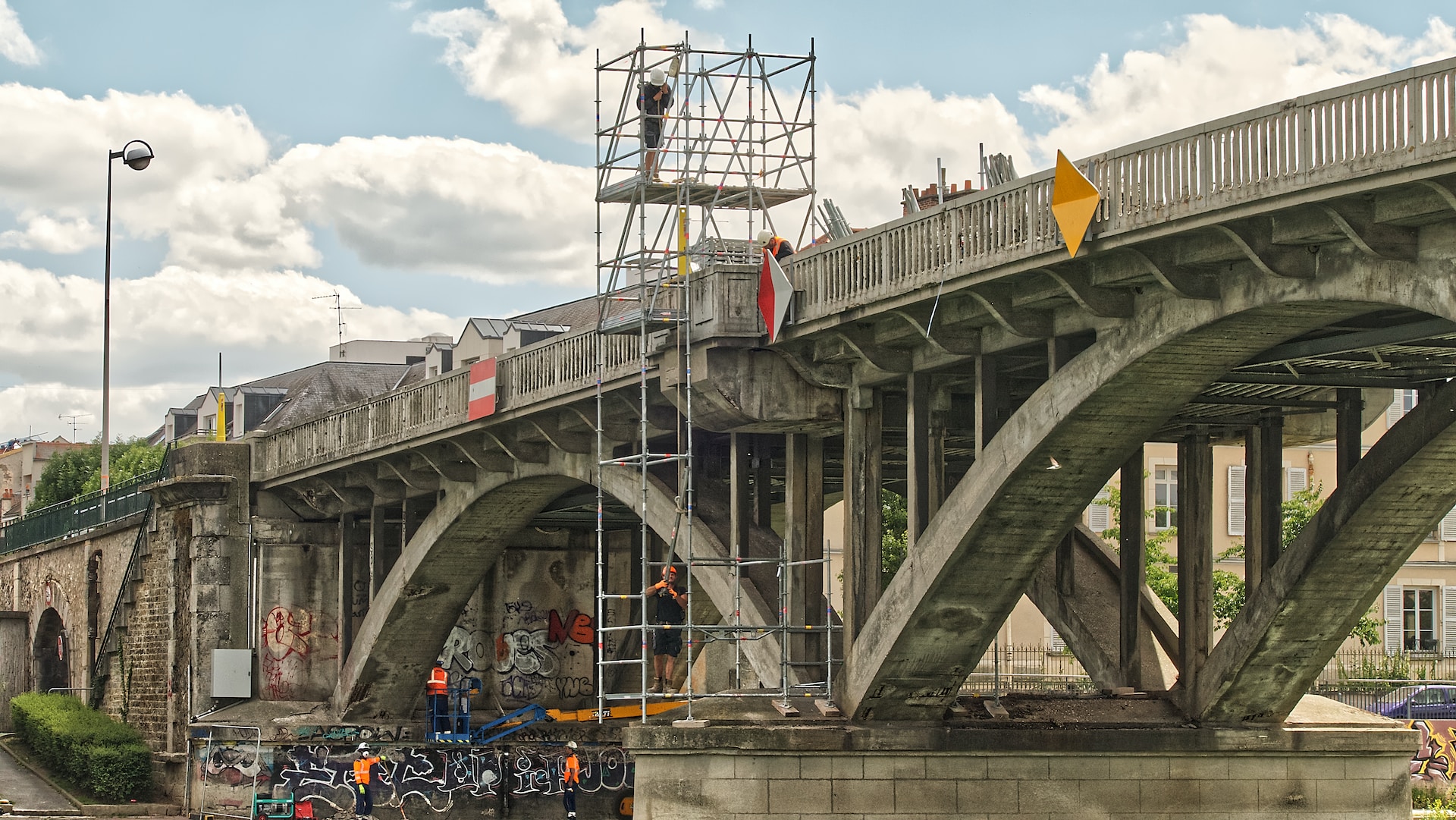 people riding on blue and black motorcycle under gray bridge during daytime